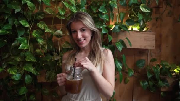 Sonriente Joven Hembra Bebiendo Tarro Cafetería Exuberante Interior — Vídeo de stock