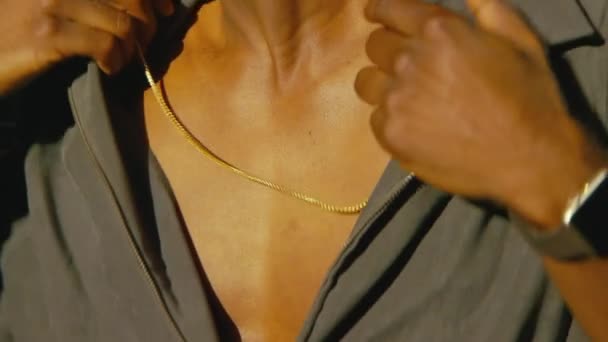 Close up shot of necklace worn by man as he adjusts his shirt