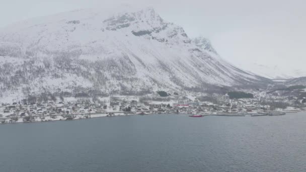 Kfjord町の中心部とノルウェーのOlderdalenの雪の山のふもとの港 オーバーキャスト冬の天候 横回転運動と4K空中ドローンショット — ストック動画