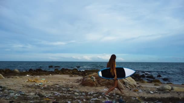 Tan Surfer Girl Holding Surfboard Walking Dirty Polluted Beach Ocean — стоковое видео