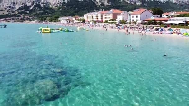 バスカビーチ クルク島 クロアチア 夏休み中の大通り 観光客 サンベッド ウォータープレイグラウンドの空中ドローンビュー 明らかに — ストック動画