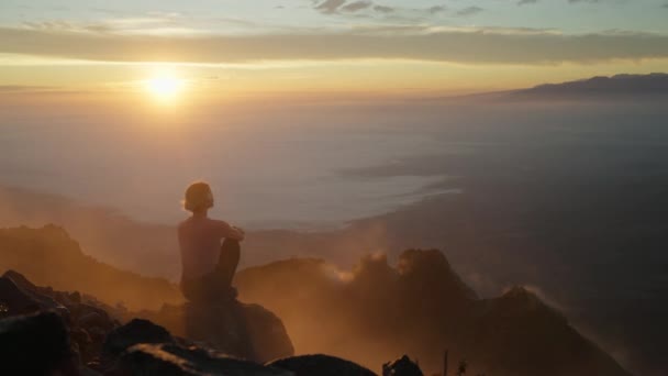 坐在岩石边缘上的女人被山顶上橙色的晨光照亮了 — 图库视频影像