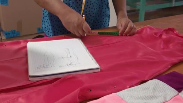ノートを取り木製のテーブルの上にドレスの措置を取るラテンファッションデザイナー — ストック動画