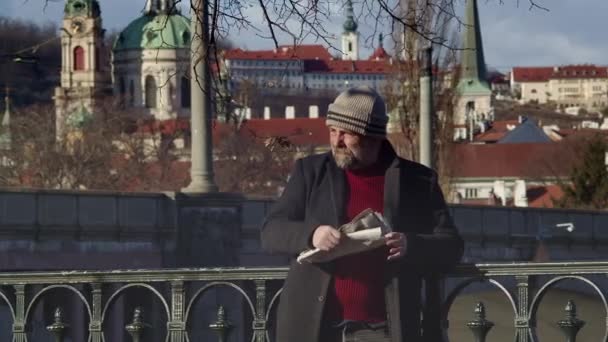 Bir Adam Okuduğu Gazeteyi Katlarken Etrafına Bakar Arka Planda Prag — Stok video