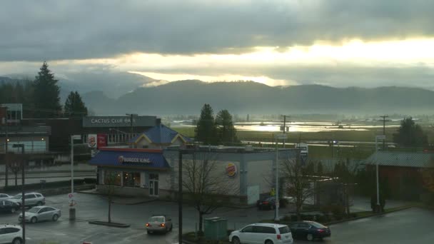 山边繁忙的郊区景色 日落时店面为店面 在加拿大不列颠哥伦比亚省Abbotsford 阳光透过令人惊奇的移动云彩景观 — 图库视频影像