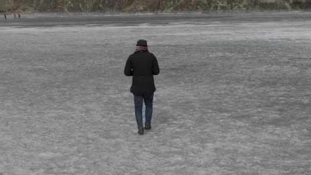 成年男子抱着钻机控制器转身走过结冰的湖前 — 图库视频影像