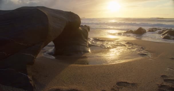 波がニューカイ州コーンウォールの日没の間に前景に海のアーチで小さな牧歌的なビーチの海岸に衝突英国 固定ショット — ストック動画