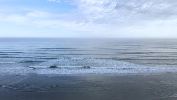 Statický záběr na pláž Nantasket v Massachusetts. Pomalé vlny, surfaři daleko v dálce za mlhavého dne pod modrou, zataženou oblohou. Letecký pohled 4k.