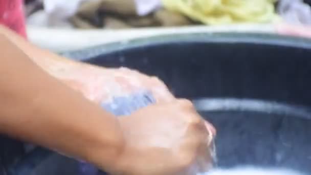Asijská žena praní oblečení. mytí a drhnutí oblečení zblízka HD video. Indonéská žena prala prádlo vedle koupelny. Ruční praní oblečení v kbelíku s mýdlovými bublinkami