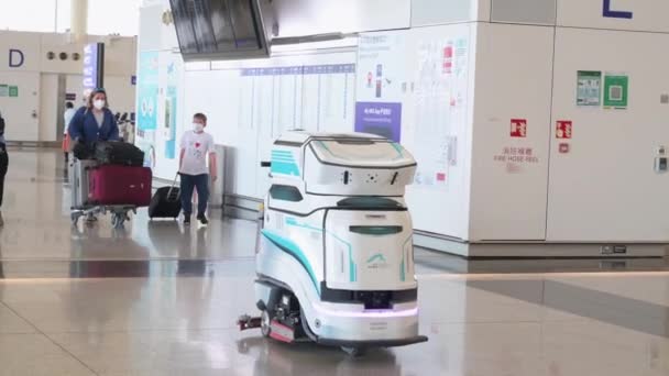 Egy autonóm fertőtlenítő és tisztító gép látható a Chek Lap Kok Nemzetközi Repülőtér érkezési csarnokában, ahogy egy fiatal utas belép Hong Kong-ba, Kínába..