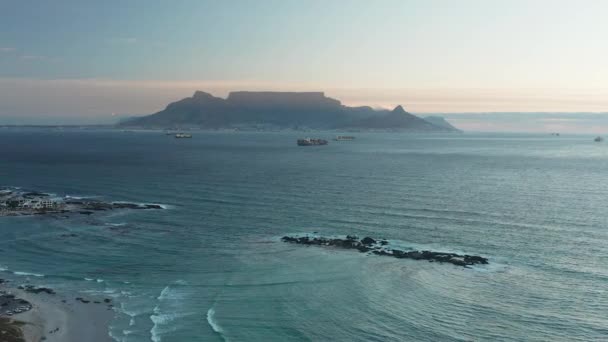 ブルバーグビーチの上のテーブルマウンテンとライオンの頭の夕日貨物船オフショア 南アフリカのケープタウン ワイドショット — ストック動画