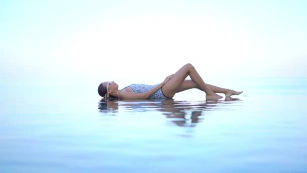 身着泳衣的女子躺在无边无际的游泳池边 与海平线和天空融为一体 — 图库视频影像