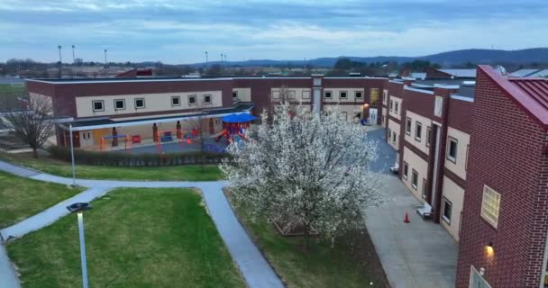 在美国的学校和学生休息的地方 空中飞过盛开的树 黎明时亮着灯 宾夕法尼亚赫希的现代红砖建筑 — 图库视频影像