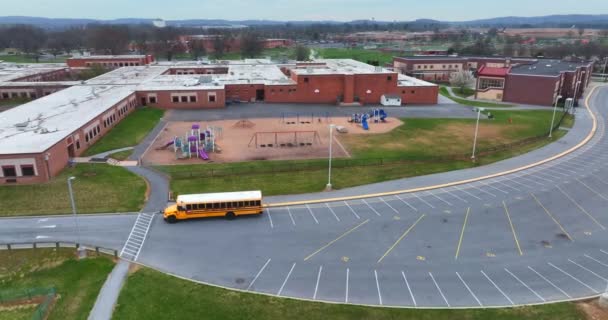 スクールバスはキャンパスで学生を待っています アメリカの建物や遊び場 空中進入の降下 — ストック動画