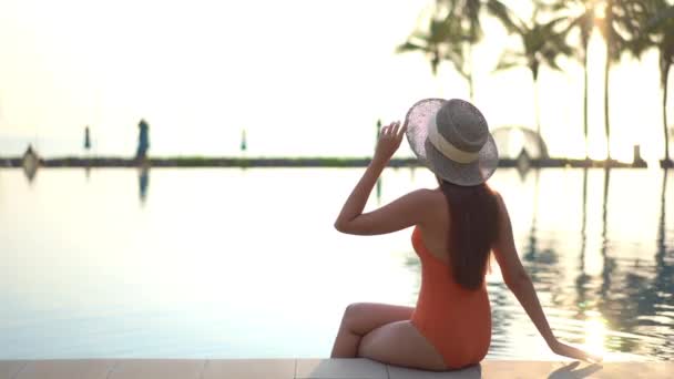 Back Camera Woman Sitting Edge Pool Reaches Adjust Her Sun — Stockvideo