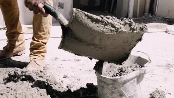Pracovník ručně nabírá cement do kbelíku s rýčem na staveništi