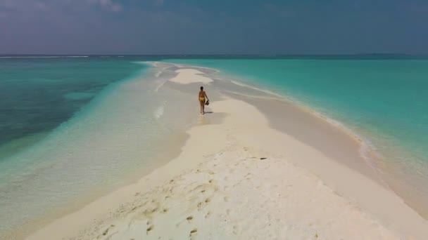一个手里拿着帽子的女孩沿着沙滩向地平线跑去 沿着被清澈的碧绿水冲刷着的沙堤走去 — 图库视频影像