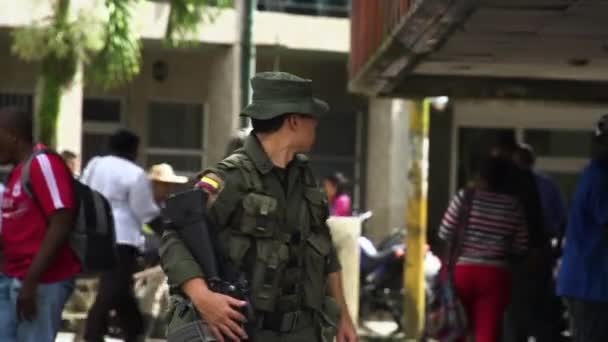 一个拿着来福枪的哥伦比亚年轻人在繁忙的街道上监视着平民 — 图库视频影像