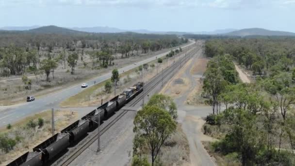 オーストラリアのクイーンズランド州バジョルの道路と平行した鉄道で走る空の石炭列車 空中ドローンビュー — ストック動画
