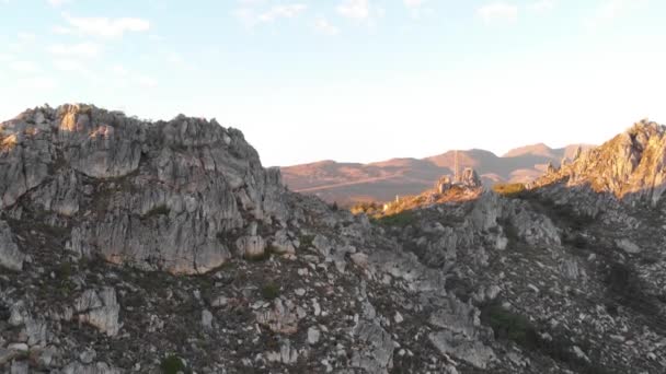 夕暮れ時の山頂の岩の風景やパワーラインを捉えた傾斜ドローンショット 手前の岩は影があり 奥の風景はライトアップされています — ストック動画