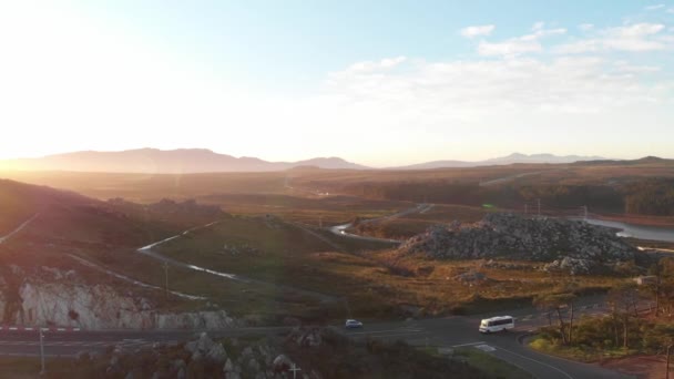 午後遅く 田舎の道路をドローンで撮影しました 太陽は沈み 空は明るく 前景と背景には輸送が見える 山が多い — ストック動画