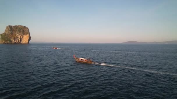 アンダマン海で日の出の間に2つのタイのロングテールボートと平行に飛行する空中ドローンとクラビの距離にある大きな石灰岩の岩タイ — ストック動画