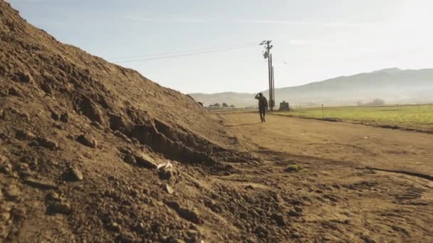 Wide Shot Man Walking Dirt Road Next Dirt Berm Farm — Stock Video