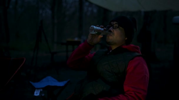 Ασιάτης Χαλαρώνοντας Ενώ Πίνοντας Ποτό Από Γυάλινο Μπουκάλι Στο Campfire — Αρχείο Βίντεο