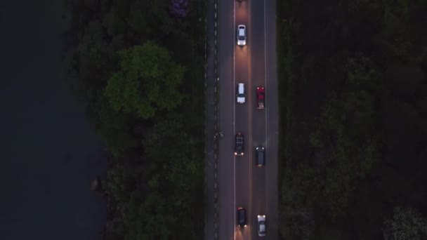 空中俯瞰使道路变得平坦 夜间有车 两边都有灯光 海边都有森林 — 图库视频影像