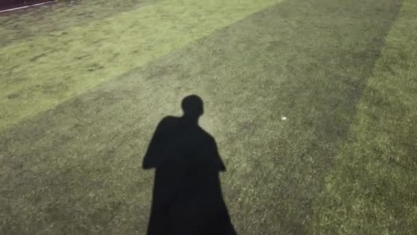 男子影子在阳光灿烂的日子里在足球场上行走的景象 — 图库视频影像