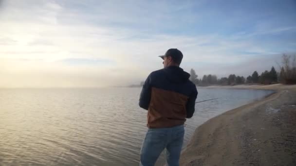 Klip Człowieka Skraju Jeziora Podczas Wschodu Słońca Rzucającego Wędkę Mgłą — Wideo stockowe