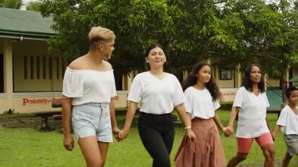 キャンパス内の芝生で手を携えて歩く幸せな若者と大人のフィリピン人 手持ちのフォローショット — ストック動画