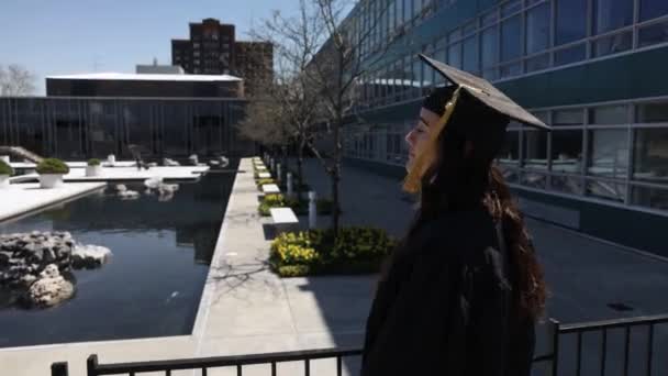 白种人女大学毕业生 头戴帽子 身穿长袍 转身对着相机 慢镜头微笑 — 图库视频影像