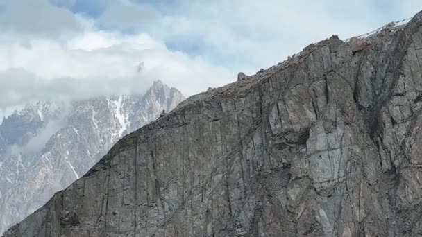 雲の中に隠れているカラコルム山脈のパスコーンを明らかにするために山の壁を渡って左の空中ドリー — ストック動画