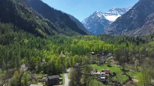 空中卡车向右展示了一个阳光灿烂的绿色山谷中的村庄 周围环绕着陡峭的高山和白雪覆盖的山峰 — 图库视频影像