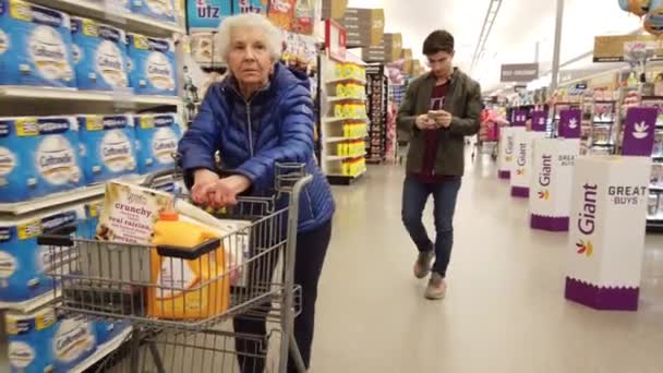 彼女の後ろに彼女の孫と一緒に食料品店でショッピングカートを押している高齢女性彼女は彼女自身を取ります — ストック動画