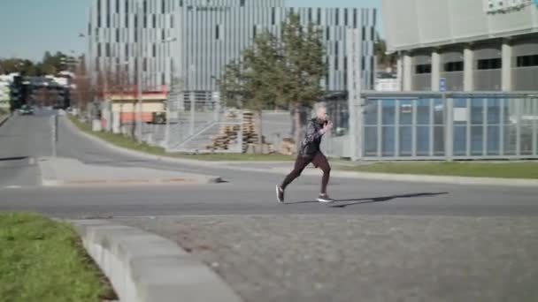 一名身穿黑衣的运动员在城市地区冲刺时手持弹弓 — 图库视频影像