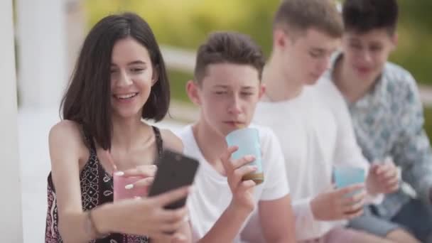 10代の女の子は男の子の前に座り ソーシャルネットワークのために自撮りします 夏休み以外でジュースを飲んで楽しむ — ストック動画