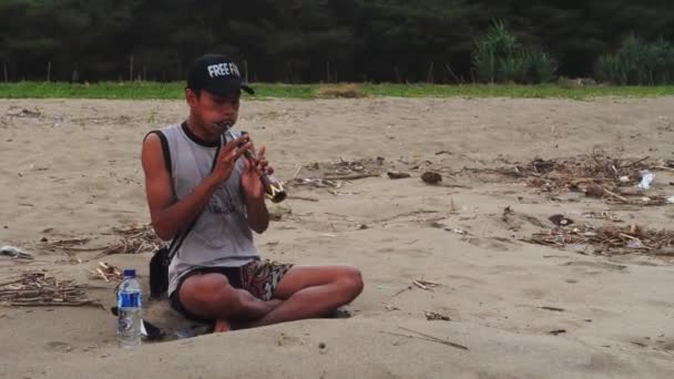 Jovem Senta Praia Areia Toca Flauta Indonésia Floresta Exuberante Fundo — Vídeo de Stock