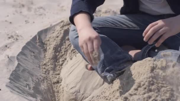 Menino Roupas Casuais Senta Pernas Cruzadas Praia Cavando Buraco Areia — Vídeo de Stock