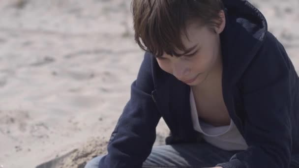 Young Boy Casual Clothing Digging Hole Sandy Beach Summertime Smiling — Vídeo de Stock