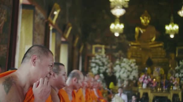 泰国曼谷佛教寺庙里的僧侣 纹身和橙色的僧人最近的相机抓挠他的脸 大的金色佛像在背景中 慢动作 — 图库视频影像
