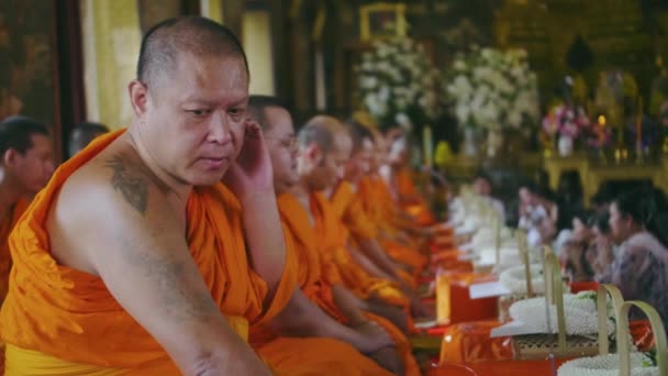 泰国曼谷寺庙里纹身佛教僧人的慢镜头 和尚转过头对着相机笑了 更多身穿橙色长袍的僧人坐在他旁边 — 图库视频影像