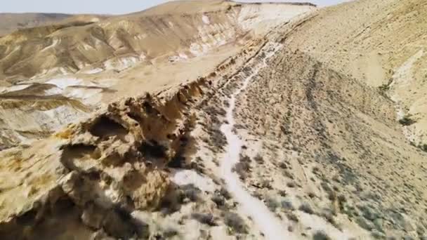 在阳光灿烂的天空中 空中低空飞越山脊 在沙漠小径上远足 展现出壮观的风景 地点是以色列内盖夫沙漠的Ramon Crater — 图库视频影像