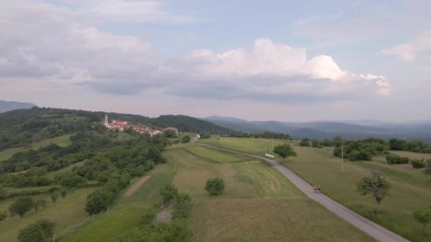 两个骑自行车的人骑着自行车走在通往村子的路上 Drone View — 图库视频影像
