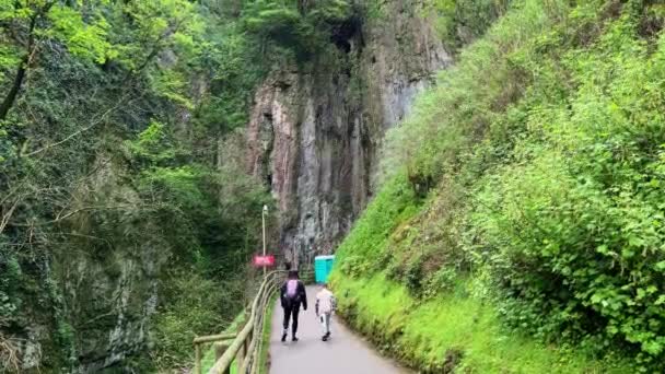 Two People Walking Pass Steep Cliffs Both Sides Green Trees — Video
