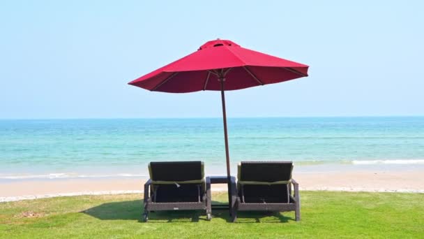赤いビーチの傘の下にある2つの空のラウンジチェアのクローズアップビーチと着信潮に直面しています — ストック動画