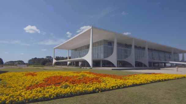 首都ブラジリアの花の美しいフィールドと緑の芝生の真ん中にパラシオ プラナルトブラジル大統領の公式職場の広いショット — ストック動画