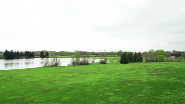 空降无人机在圆盘高尔夫球场上空向远处的一个湖和高速公路飞去 那里是早春时节 绿油油的 — 图库视频影像