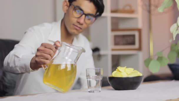 一个穿着衬衫的年轻人在家里把苹果汁倒入杯子里 — 图库视频影像
